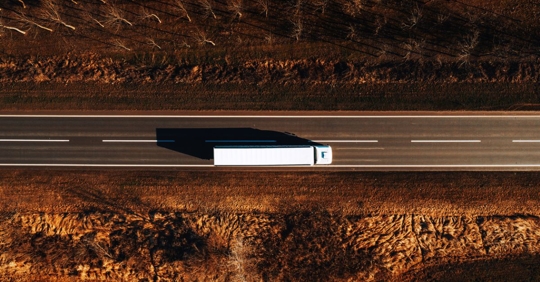 Photo from a bird's-eye-view of a white tractor trailer driving on a 2-lane highway.