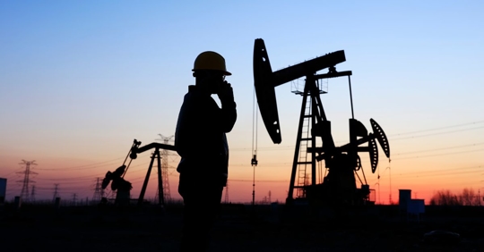 Shadow of a person in a hardhat, on their phone, with an oil pump in the background